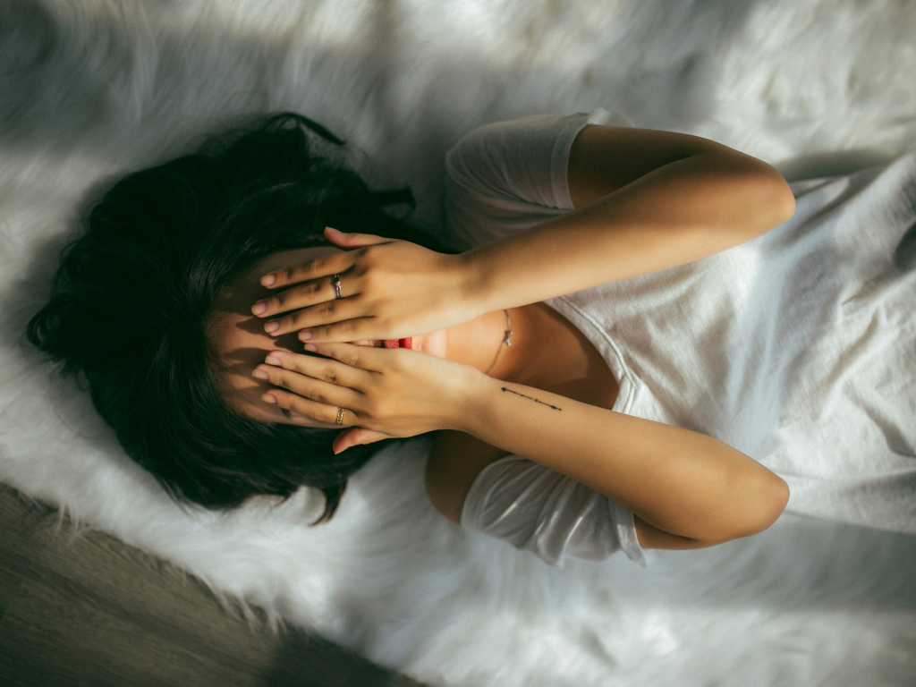 A woman lies on a white rug, hands covering her eyes, with a King Koil mattress visible in the background.
